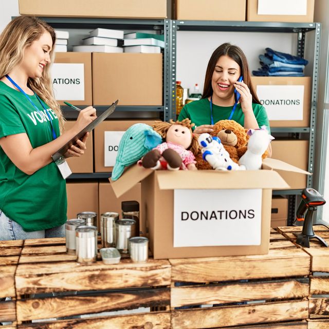 Photo: Two volunteers in green shirts sorting donated toys and goods behind a donations table