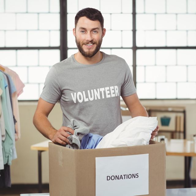 Photo: Smiling man in a gray volunteer t-shirt sorting clothes into a donations box