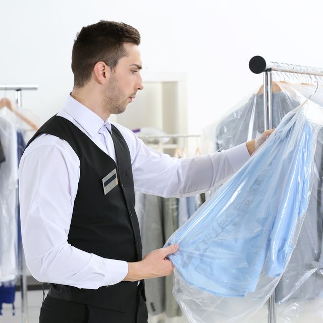 Photo: Man in a black vest and white shirt lifting a shirt in a clear plastic cover from a clothing rack