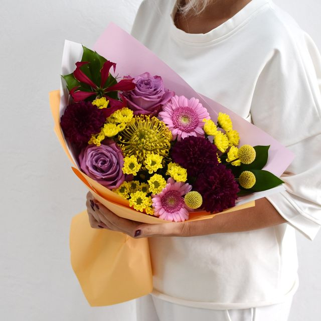 Photo: Person in a white sweater holding a colorful bouquet of flowers wrapped in pink paper