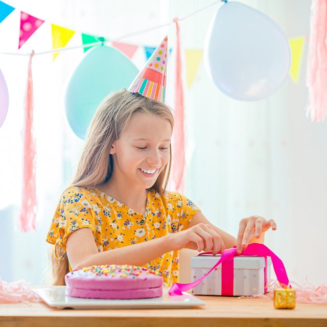 Photo: Smiling girl wrapping a gift next to a birthday cake under party flags