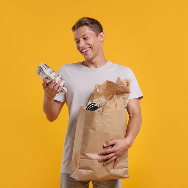 Photo: Smiling man holding a brown paper bag of pet food against a yellow background