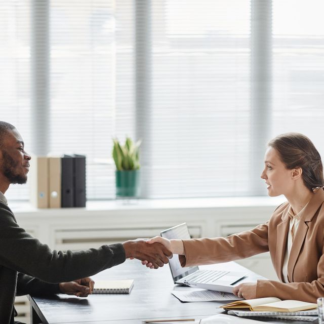 Photo: Man and woman shaking hands across a desk in a bright office