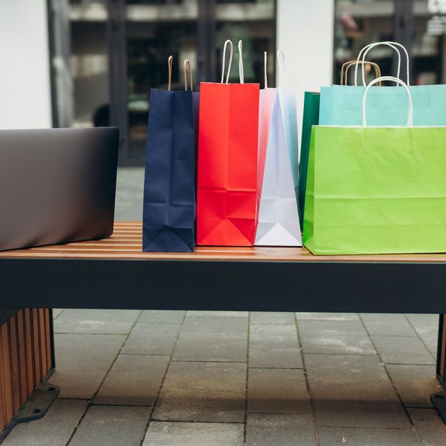 Photo: Colorful paper shopping bags and a laptop on an outdoor bench