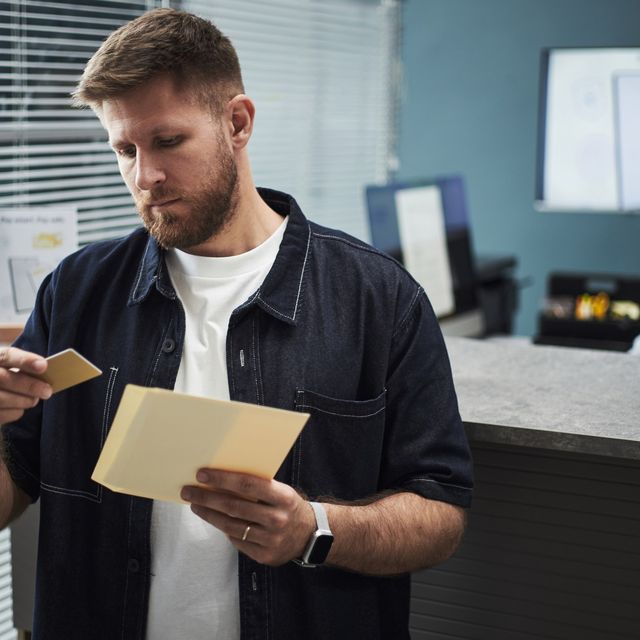 Photo: Man in a dark jacket looking at a tan envelope in an office reception area
