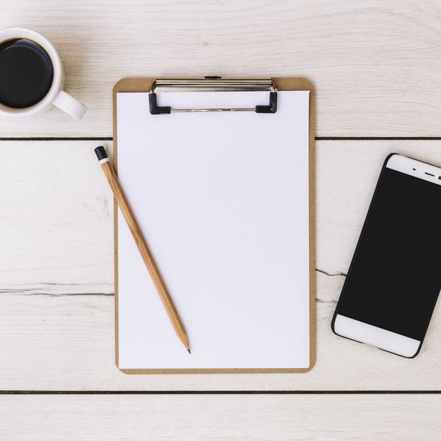 Photo: Clipboard with blank paper, a pencil and a smartphone on a white wooden table beside a coffee cup