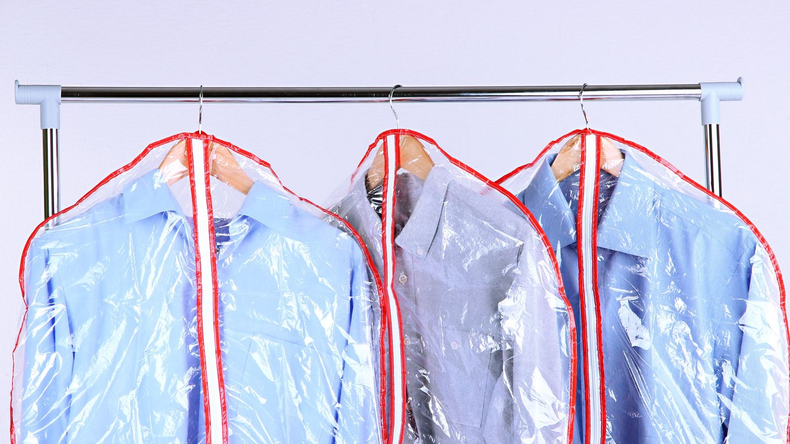Three shirts hanging in clear dry cleaning garment covers with red trim on a metal rack