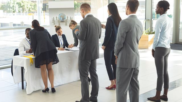 People in business clothes standing in line at a registration table in a bright lobby