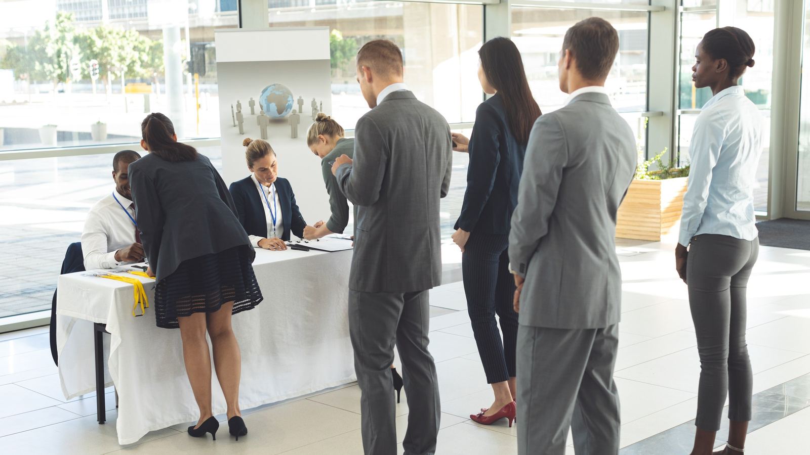 People in business clothes standing in line at a registration table in a bright lobby